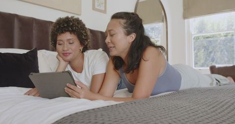 Friends relaxing on bed enjoying tablet entertainment