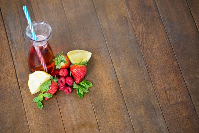 Refreshing berry cocktail with fresh strawberries, raspberries, lemon slices, and mint leaves on wooden table. Perfect for summer beverage promotions, healthy drink advertisements, and detox water recipes.
