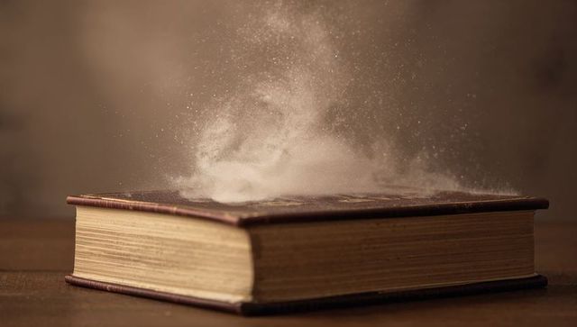 Vintage hardcover book releasing dust cloud with gilded edges and sepia haze