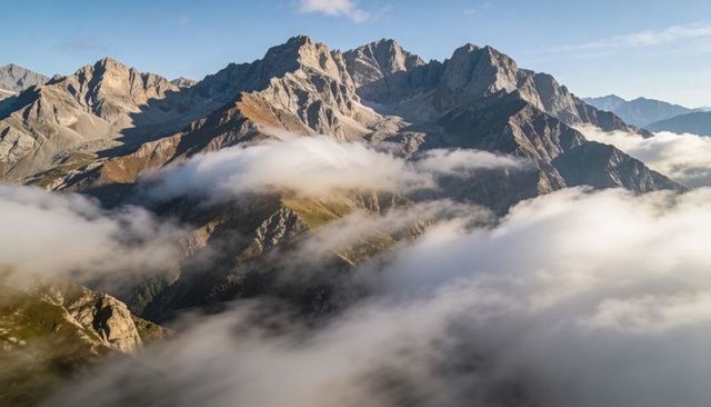 Sunlit jagged alpine massif rising above swirling valley fog with rugged ridges and peaks