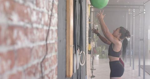 Female athlete throwing green medicine ball against brick wall during partner workout