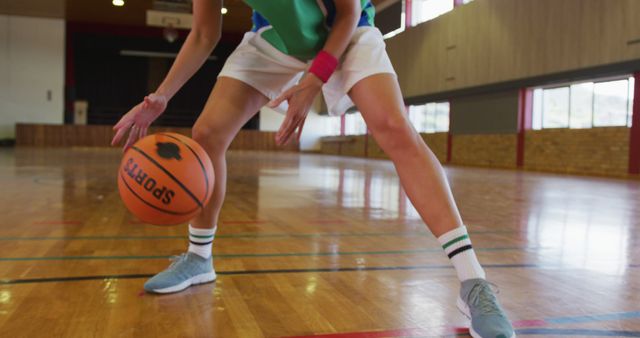 Person dribbling basketball indoors, emphasizing athletic skill and focus. Ideal for use in sports-related content, fitness articles, teamwork campaigns, and healthy lifestyle promotions. Common setting for gym or school sports events.