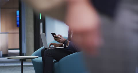 Businessman Using Smartphone and Laptop in Modern Office