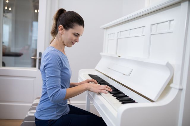 Woman playing piano at home, wearing casual clothes. Ideal for concepts related to music practice, hobbies, home activities, and concentration.