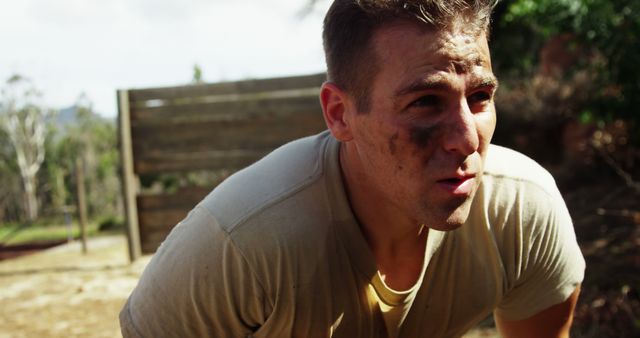 Male soldier engaging in intense outdoor training exercise with determinate expression wearing t-shirt and dirty face marks. Useful for themes related to military, physical fitness, perseverance and challenging environments.
