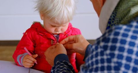 Father assisting daughter in red jacket at home table