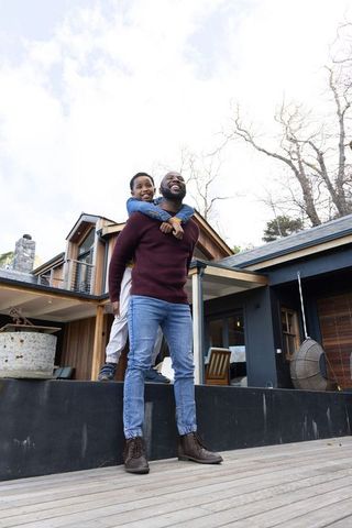 African american father giving piggyback to son on modern rustic deck