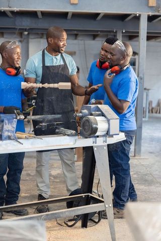 African american mentor teaching apprentices wood lathe turning in carpentry workshop