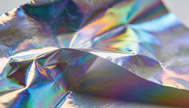 Crumpled holographic foil reflecting rainbow light abstract metallic texture background