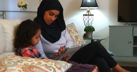 Hijabi Mother and Daughter Bonding on Sofa with Tablet