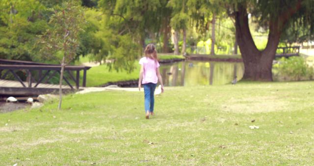 Little girl walking away in green park holding toy, surrounded by trees and nature. Perfect for depicting peaceful moments, childhood adventure, outdoor activities, and solitude in nature. Suitable for articles about parenting, mental wellness, and recreational activities for children.