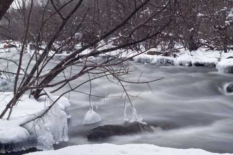 Frozen river flowing through snow-covered banks with icicles and bare winter branches