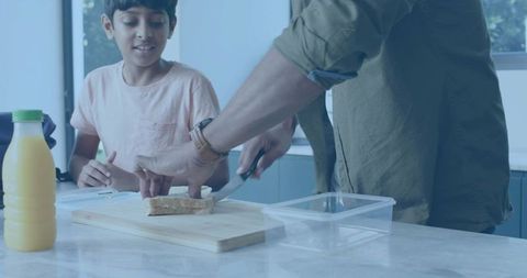 Dad preparing school lunch: father slicing sandwich on marble counter while son watches