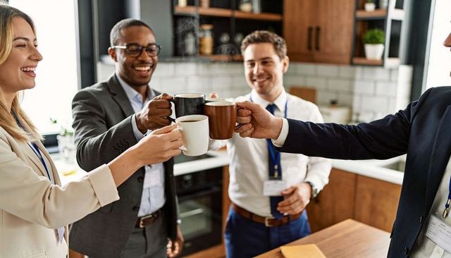 Business colleagues clinking coffee mugs at modern kitchen island celebrating teamwork
