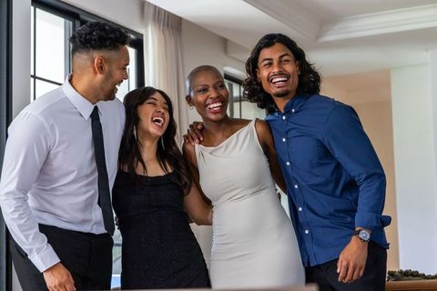 Laughing friends in semi-formal outfits celebrating at sunlit modern living room gathering
