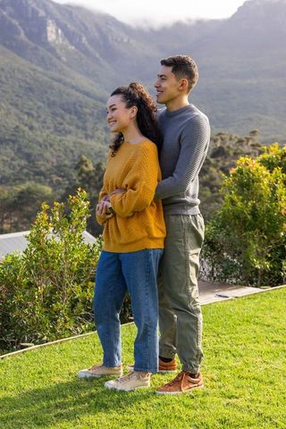 Asian couple embracing on grassy overlook, cozy knit sweaters, mountain valley vista