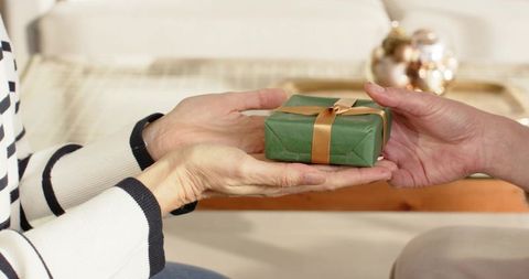 Mature and mid-adult women exchanging green gift wrapped with gold ribbon on coffee table