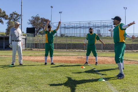 Amateur baseball team stretching on infield with coach signaling cones preseason warmup