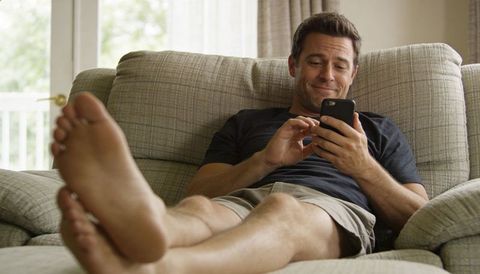 Relaxing man on couch using smartphone and smiling in bright living room