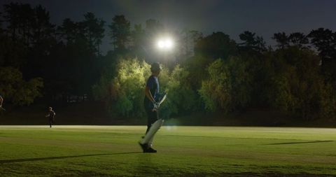 Floodlit night cricket with diverse teammates sprinting between wickets on grass pitch