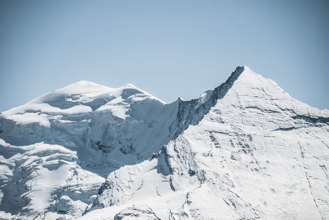 Snow-covered mountains against a clear blue sky creating a serene and inviting landscape. Ideal for use in travel brochures to promote winter destinations, adventure and nature blogs, and serene wallpapers.