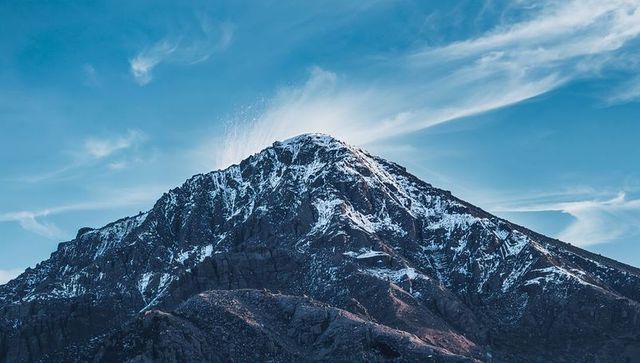 Sunlit Alpine Peak Rising Over Rugged Snow-Covered Crags with Haloed Sky and Cirrus Clouds