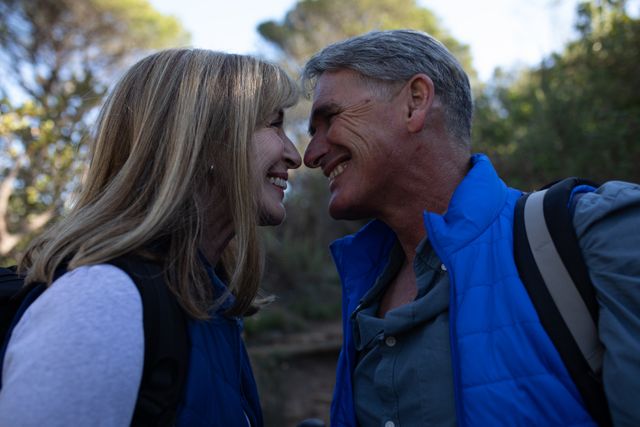 Senior couple enjoying a hike in the mountains, sharing a loving moment while smiling at each other. Ideal for use in advertisements promoting active lifestyles, retirement communities, travel agencies, and health and wellness products. Highlights themes of love, happiness, and outdoor adventure.