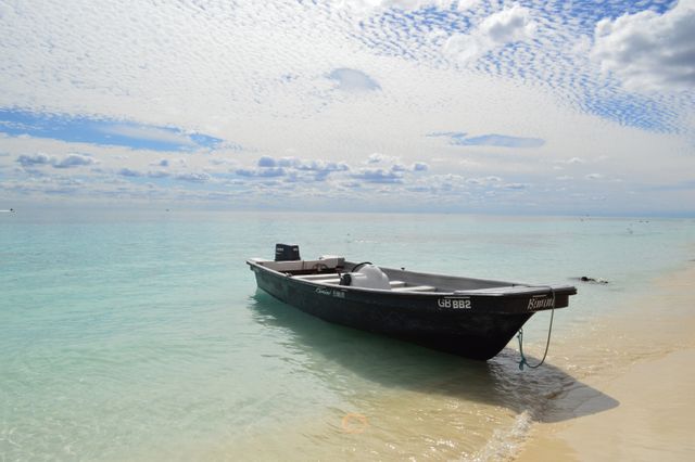 Single boat resting on a calm tropical beach with crystal clear waters and a beautiful azure sky. Ideal for travel brochures, vacation advertisements, or wallpapers promoting serene beach getaways and tranquil holidays.