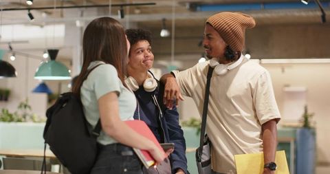 Diverse college students chatting in modern campus lounge with notebooks and headphones