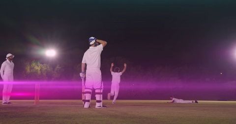 Night cricket action under floodlights showing batter holding bat and bowler celebrating