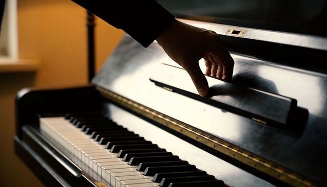 Hand lifting piano fallboard over glossy upright keyboard in warm interior light