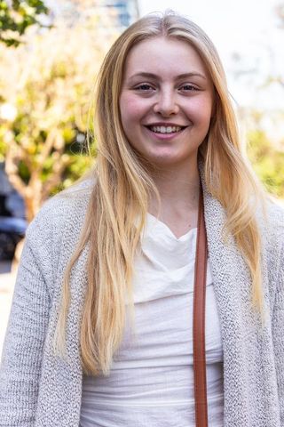 Young blonde woman smiling on urban street wearing gray cardigan and crossbody strap