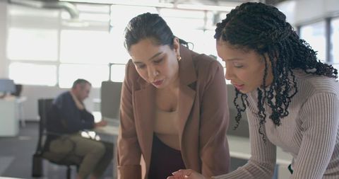 Diverse colleagues leaning over desk reviewing tablet and collaborating in open-plan office