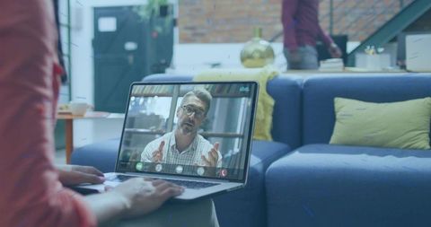 Typing woman on laptop during remote video call in modern living room with sofa and bookshelf
