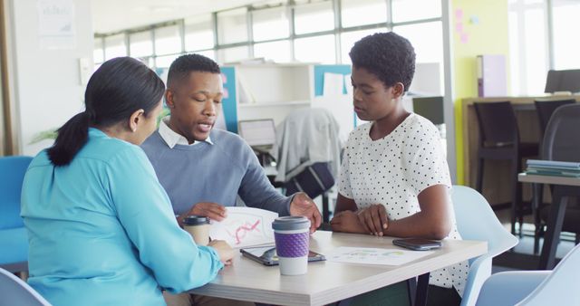 Three business professionals are discussing a project around an office table. Two women and one man are focusing on a document, showcasing teamwork and collaboration. Ideal for illustrating business meetings, professional collaboration, and corporate culture.
