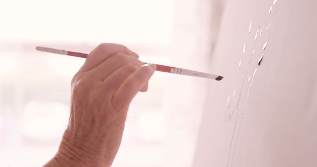Close-up of an artist's hand painting on canvas with a paintbrush. Useful for illustrating creativity, artistic hobbies, fine art techniques, and hands-on activities. Ideal for art supplies advertisements, art class promotions, and creative process illustrations.