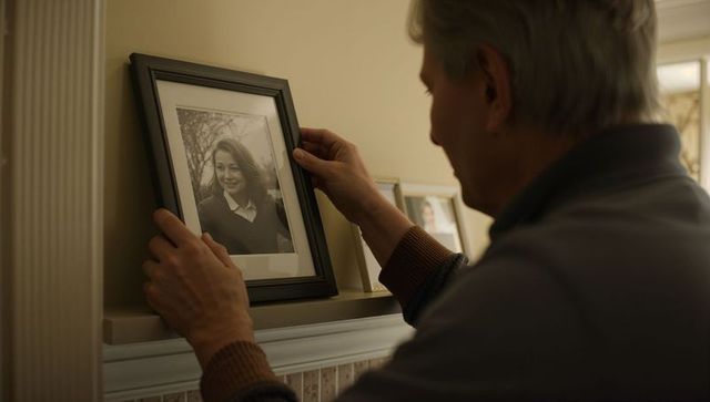 Senior man adjusting framed portrait on mantelpiece, nostalgic moment and home memories