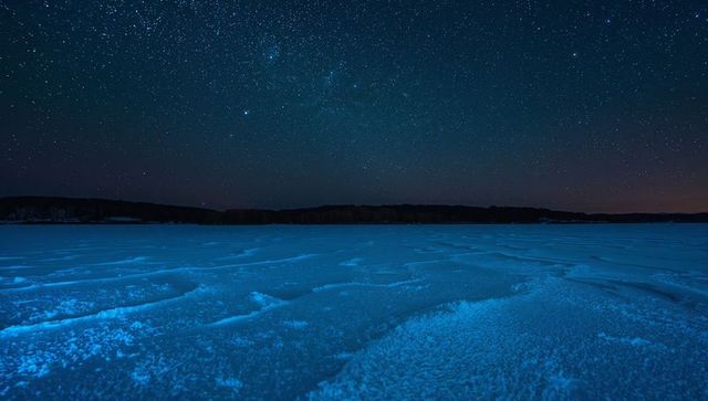 Glowing blue frozen plain under milky way night sky, icy ridges and frosty texture