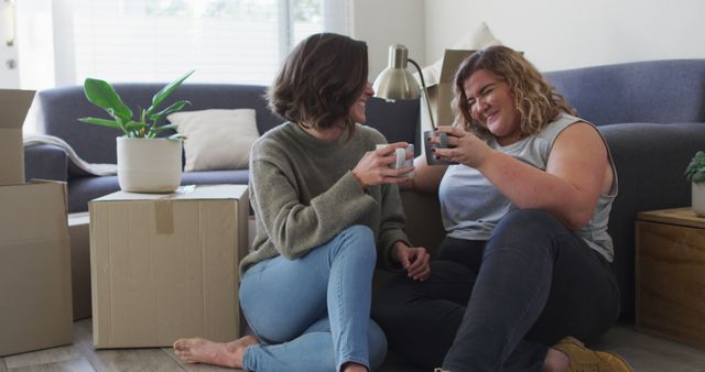 Caucasian happy lesbian couple drinking tea sitting on floor in new home. domestic life and leisure time.