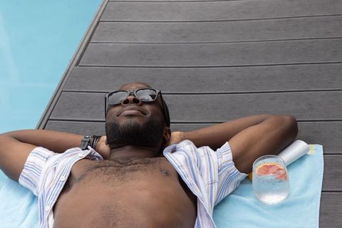 African american man relaxing on poolside lounger with sunglasses and citrus drink