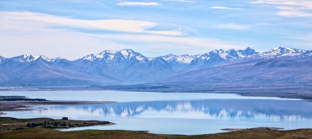 Beautiful landscape featuring towering mountains reflecting on a calm, tranquil lake under an expansive blue sky. Ideal for promoting travel, environmental conservation, or serene backgrounds in presentations. Perfect for use in magazine spreads, travel brochures, websites, and inspirational posters.