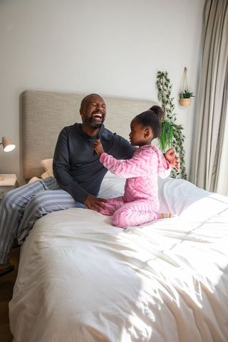 African american father and daughter laughing, playfully grooming on bed in cozy morning