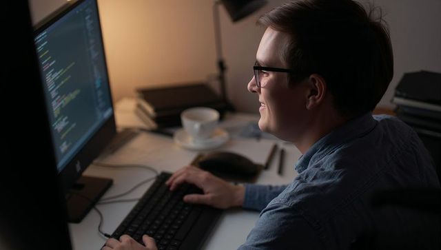 Developer in home office typing code on large monitor