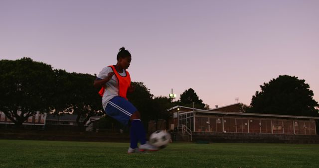 Biracial female football player kicking ball on field, unaltered with copy space. Sports, competition, football and teamwork concept.