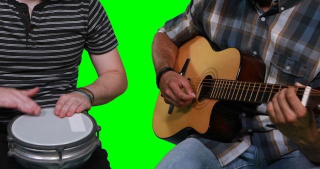 Mid section of male musicians playing guitar and drum against green screen
