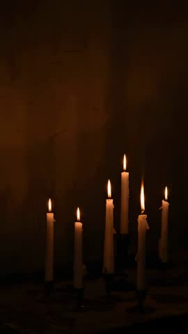 Vertical video flickering taper candles melting wax on rustic tabletop warm contemplative glow