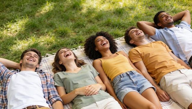 Group of friends laughing and relaxing on picnic blanket in sunny park summer lifestyle