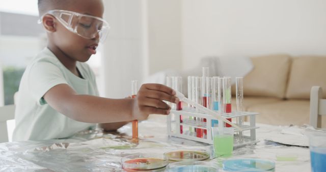 Young African American boy conducting a scientific experiment at home with various test tubes and a pipette. Appears engaged and focused on the activity. Perfect for education materials, children's STEM programs, homeschool resources, and promoting science activities for kids.
