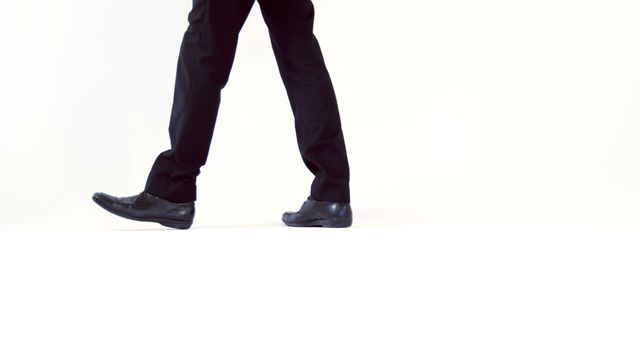 A person in black trousers and dress shoes is walking, with copy space. Capturing just the lower half of the body, the image emphasizes movement and direction.
