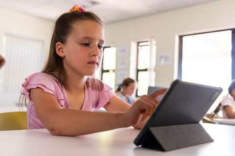 Elementary girl engaging with tablet for focused digital learning in bright classroom